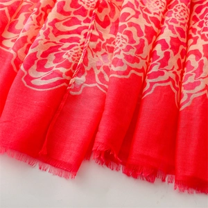 Close-up of lightweight red scarf featuring large orange floral prints and frayed edges