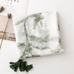 Detail of white cotton scarf with green tropical leaf prints and decorative tassels