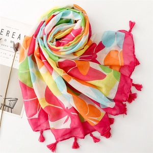 Close-up of vibrant floral scarf with pink tassels next to lifestyle magazine and dried flowers