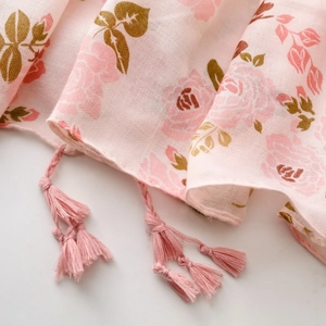 Gros plan détaillé du motif floral rose et des franges à glands sur l'écharpe en coton