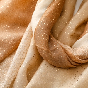 Macro shot of gold foil star pattern on beige gradient cotton linen texture scarf