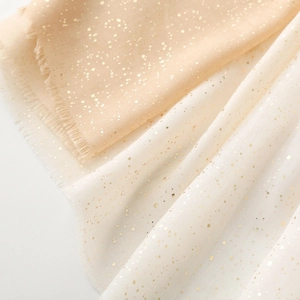 Macro detail of champagne linen-touch scarf with gold foil dots and frayed edge finish