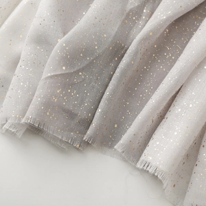 Detailed close-up of light gray cotton-linen scarf featuring gold foil dots and raw edges
