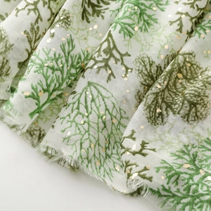 Detailed view of white linen-feel scarf with green coral pattern and gold glitter accents