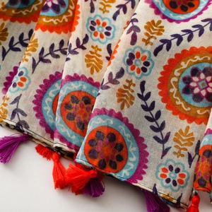 Détail d'une écharpe bohème aux motifs mandala colorés et finitions à pompons orange