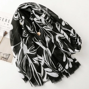 Long black and white scarf with abstract leaf prints and fringe edges on white surface