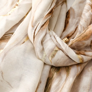 Detailed macro view of cream scarf with gold foil accents and marble pattern texture