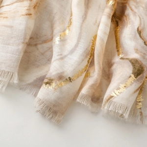Close-up of cream linen scarf with gold foil marble pattern and raw fringe edges