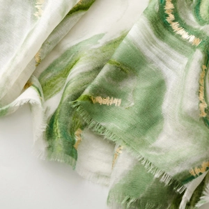Detail of green and white linen scarf featuring gold foil print and frayed edges