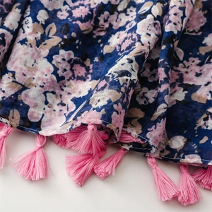 Dettaglio ravvicinato della sciarpa floreale blu con nappe rosa e trama del tessuto fine