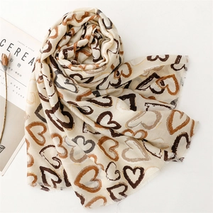 Detail of light beige scarf featuring brown heart patterns and soft frayed fringe edges