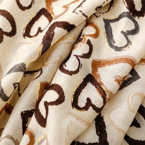 Detail of soft beige cotton linen scarf featuring metallic gold heart print and frayed edges
