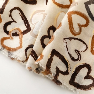 Detail of soft linen-feel scarf featuring gold foil heart patterns and frayed edges