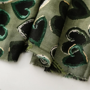 Detail of green linen feel scarf featuring gold foil heart prints and frayed edges