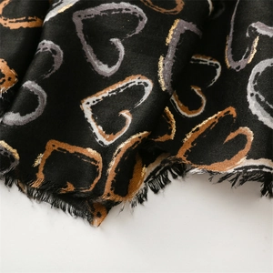 Macro detail of black cotton scarf with gold heart prints and fringe edges