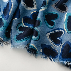 Detailed close-up of blue linen scarf featuring gold heart prints and frayed fringe edges