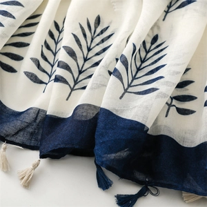 Detailed texture of blue botanical prints and cotton-linen tassel trim on a white shawl