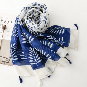 Detail of blue and white scarf with leaf patterns and handmade tassels on soft fabric