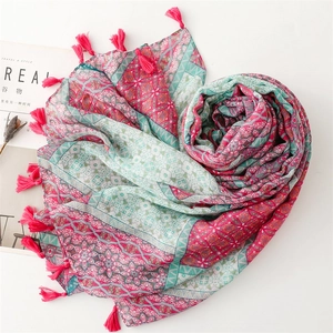 Dettaglio di sciarpa boho rosa e verde con stampe geometriche e bordi a nappa