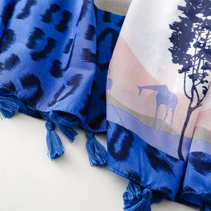 Detail of leopard print and giraffe landscape patterns with blue tassel charms on a scarf