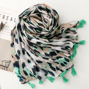 Close-up of lightweight leopard print scarf with mint green fringes on a minimal background