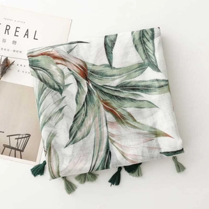 Detail of tropical green leaf print scarf with tassels beside a magazine setup