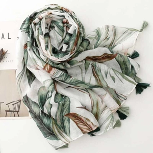 Detail of tropical palm leaf print scarf with dark green tassels on a cream background