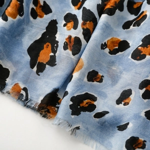 Detailed macro view of soft blue cotton scarf with orange and black leopard print and frayed edges