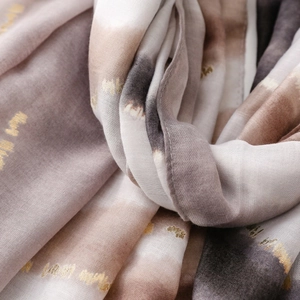 Détail macro de l'écharpe montrant des motifs dorés et un tissu dégradé effet lin