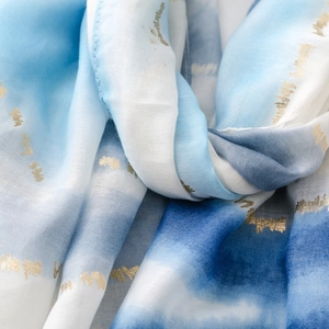 Détail d'une écharpe dégradé bleu clair avec texture dorée élégante et drapé fluide doux