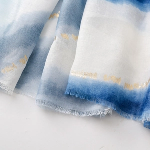 Détail d'une écharpe dégradée bleue et blanche avec dorure et bords à franges