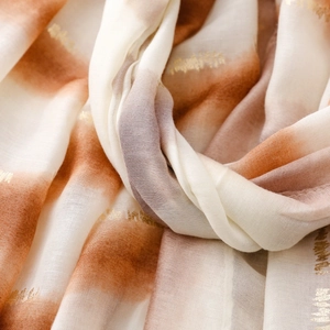 Détail d'une écharpe orange dégradé avec des motifs dorés et une texture douce