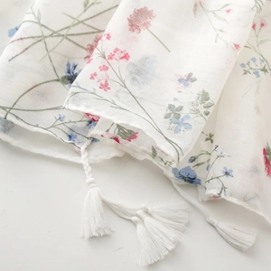 Close-up of white floral scarf featuring delicate pink blossoms and handmade tassels