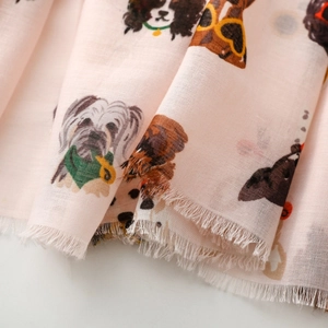Detail of light pink scarf with dog prints and natural fringe edges on soft fabric