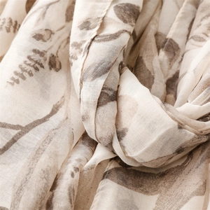 Detail of soft linen-feel scarf showing elegant brown floral patterns and tassel texture