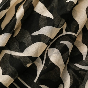 Detailed macro view of linen cotton scarf fabric with black leaf patterns and fringe