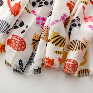 Detailed view of white cotton scarf featuring colorful cartoon cat prints and frayed edges