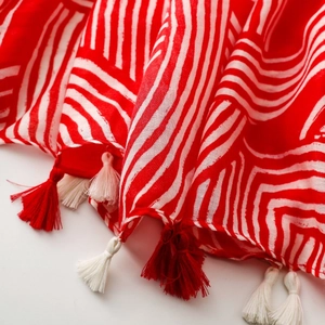 Detailed view of red and beige linen-feel scarf with multicolor decorative tassels