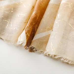 Dettaglio ravvicinato di sciarpa in cotone e lino con marmorizzazione dorata e frange