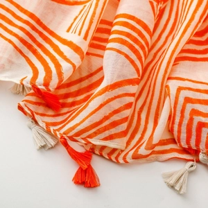Detailed close-up of soft linen-touch scarf with orange artistic lines and tassel fringe