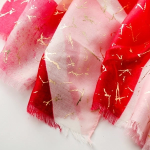 Dettaglio macro della sciarpa effetto lino rosso e rosa con decori dorati e frange