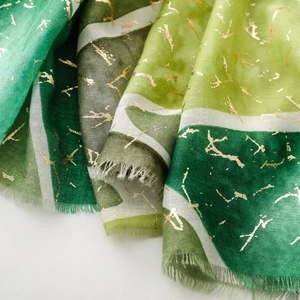 Dettaglio di sciarpa sfumata verde con accenti dorati e bordi a frange fini