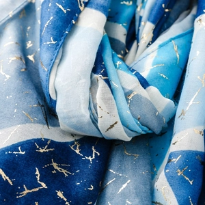Dettaglio di sciarpa blu e bianca con motivi dorati astratti e trama di lino