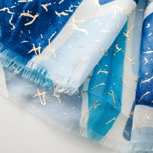 Dettaglio di sciarpa in cotone e lino blu con stampa in oro e bordi con frange