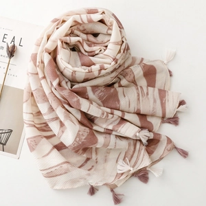 Detail of elegant cream scarf with brown marble pattern and dual-color tassels on a desk