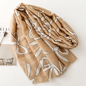 Detail of camel scarf with white bow prints and fringe edge next to a cereal magazine