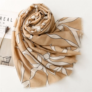 Detailed view of beige scarf featuring white leaf patterns and natural frayed edges