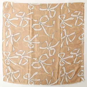 Detail of camel colored scarf featuring minimalist white bow print and frayed edges