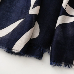 Detailed macro view of navy blue scarf featuring white leaf prints and frayed fringe edges