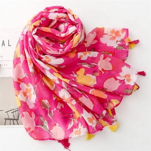 Détail d'une écharpe fleurie rose avec des glands jaune et rose sur fond blanc pur